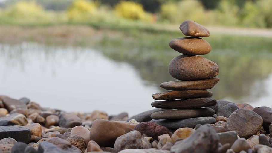 A person balancing a stack of seven rocks on their head near a body of water.