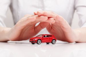 A pair of hands is shown protecting a red toy car, symbolizing car insurance protection for vehicle financial security.