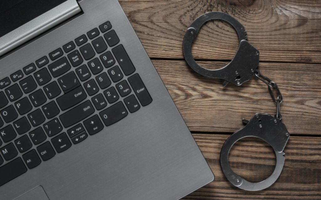 Laptop and handcuffs on a wooden table symbolizing the consequences of selling financed goods before full repayment.