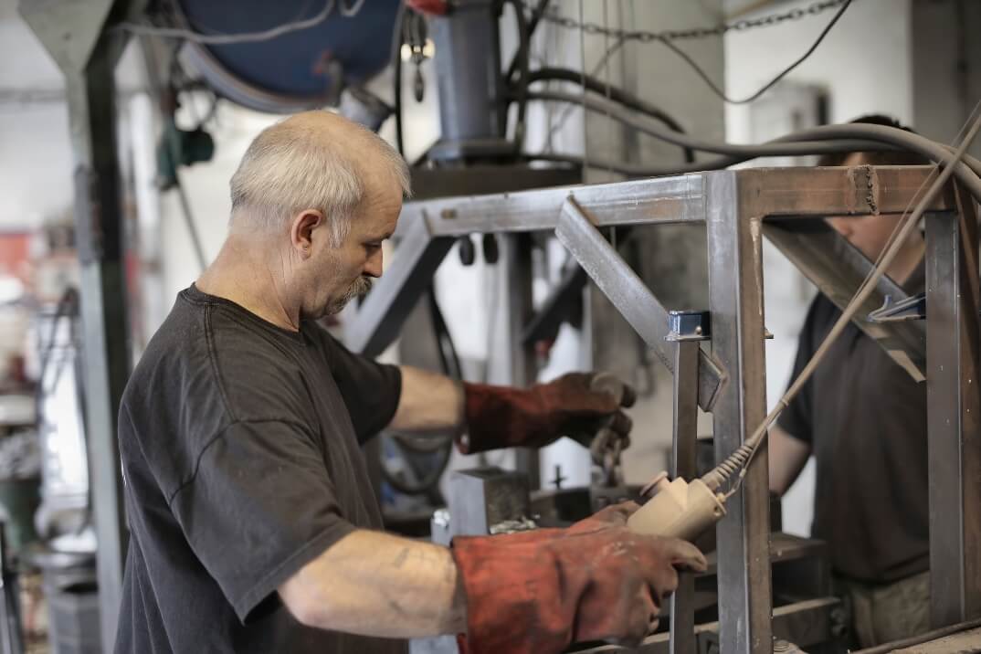 A man wearing a black shirt and red gloves operates a machine in a factory.