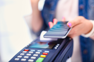 A woman is holding a smartphone over a payment terminal to pay with NFC technology.