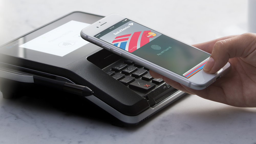 A person holding an iPhone is paying with Apple Pay at a payment terminal.