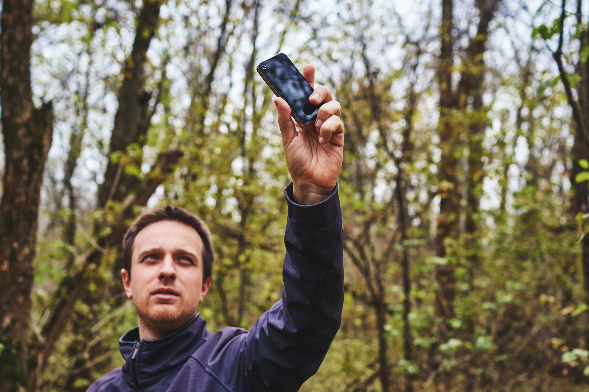 A man holds up his phone in the air in a remote area to try and get a better signal.