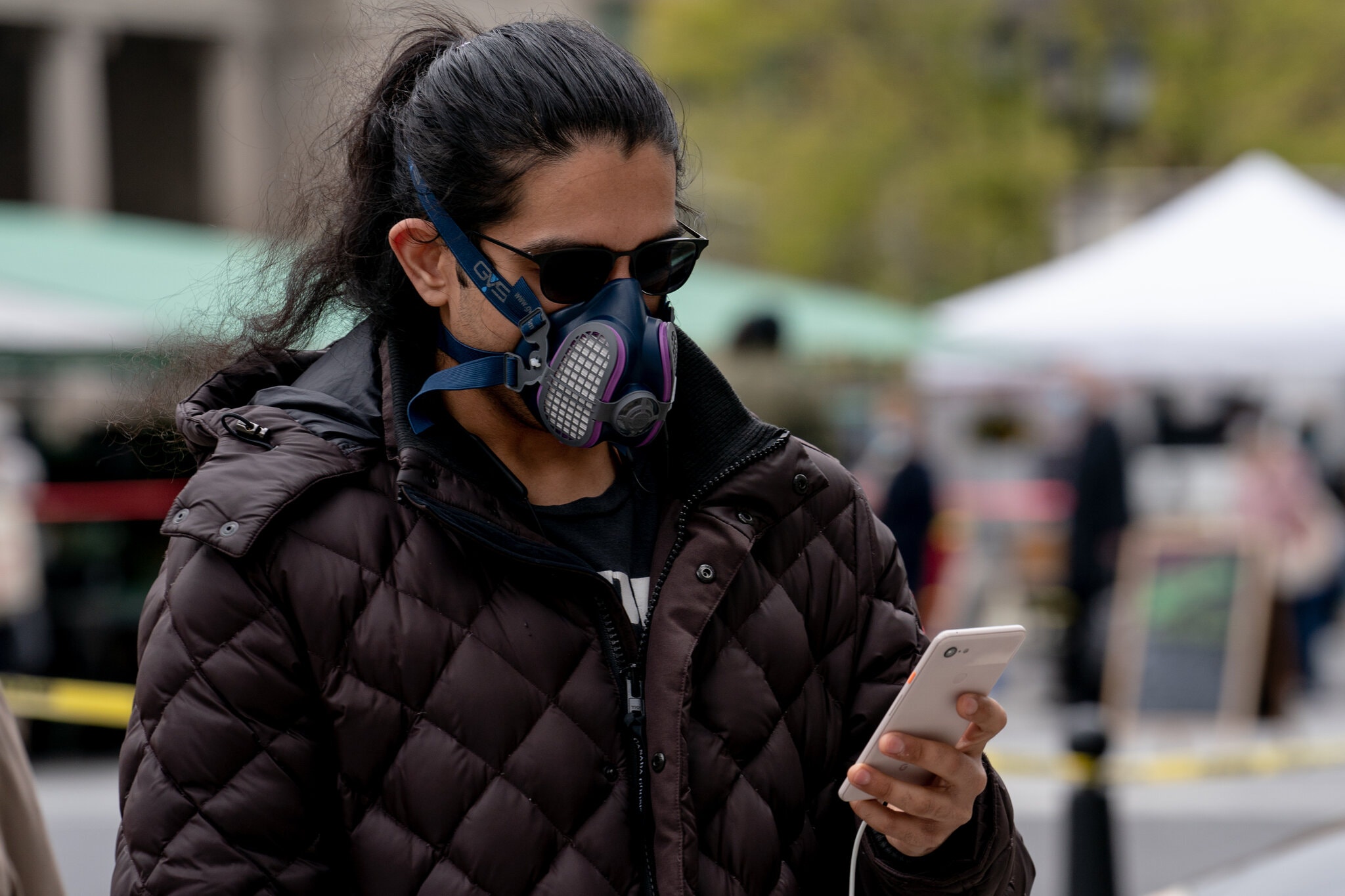 A person wearing a mask and sunglasses is using a smartphone with a location tracking app icon on the screen.
