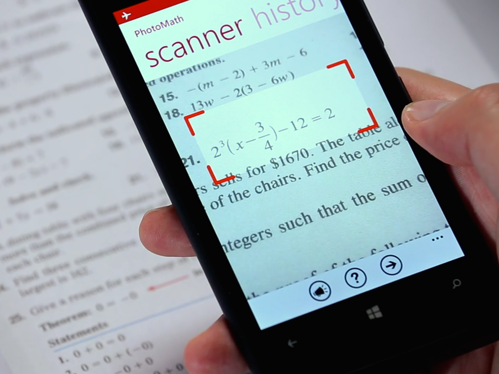 A hand holding a smartphone with the PhotoMath app open, which can solve math problems by taking a picture of them.