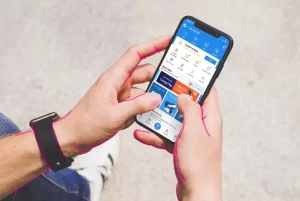 A hand holding a smartphone with the DANA app open on the screen and another hand touching the screen.