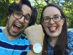A man and a woman are smiling with excitement at the camera with the woman showing off a watch on her wrist.
